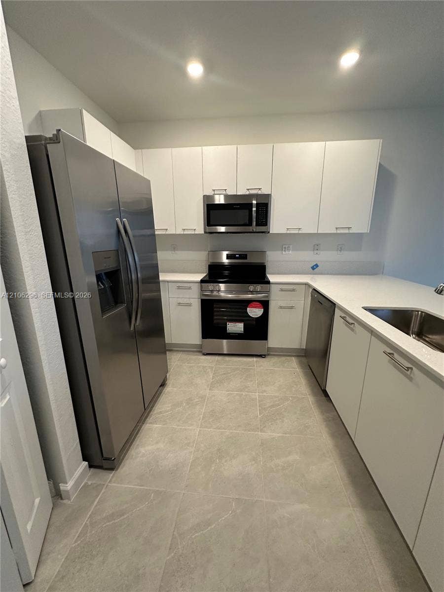 12103 NW 24th Place, #12103, Miami, Miami, FL 33167 Kitchen featuring flat-panel white cabinetry, white stone countertops, stainless steel appliances, and large-format tile flooring