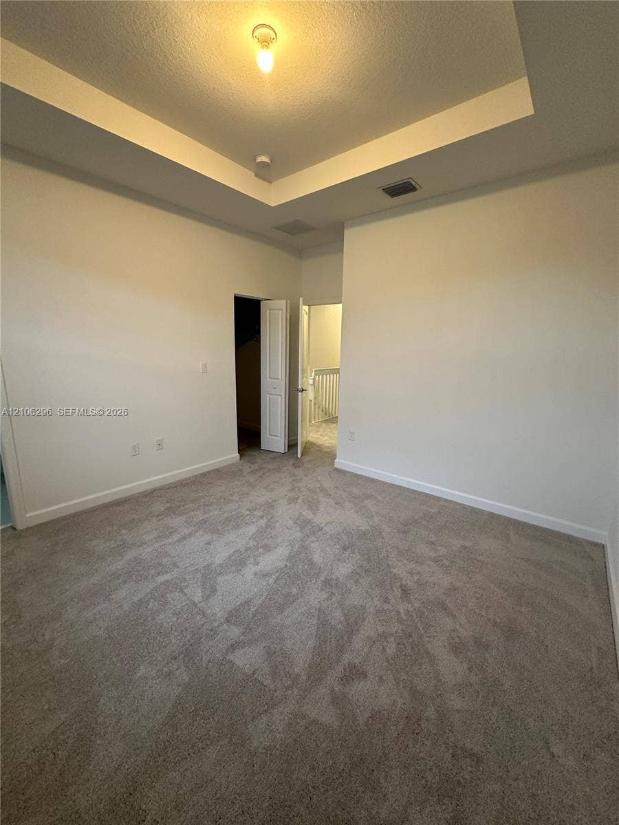 12103 NW 24th Place, #12103, Miami, Miami, FL 33167 Room featuring a tray ceiling, wall-to-wall carpeting, and an interior door leading to a closet space