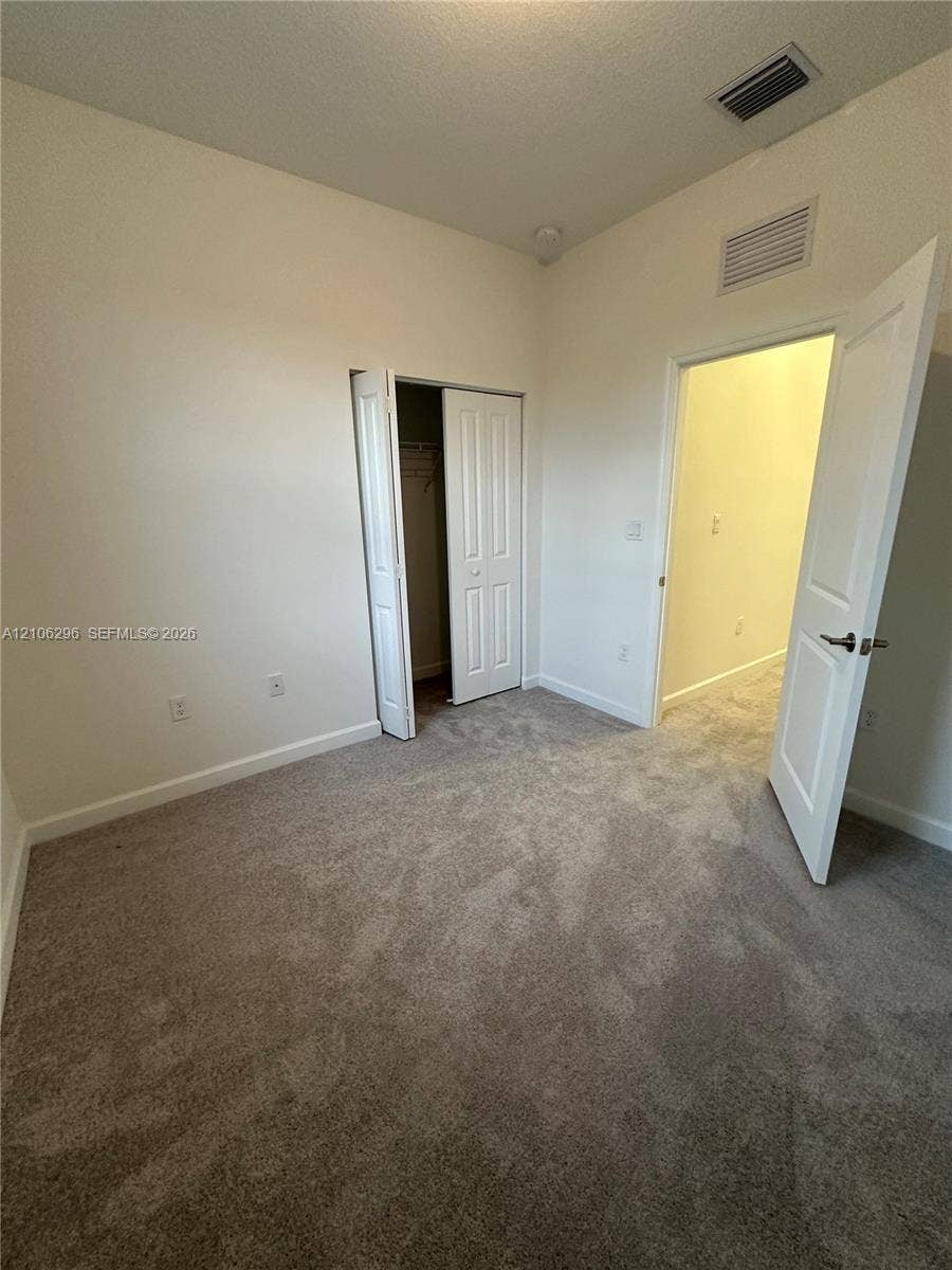 12103 NW 24th Place, #12103, Miami, Miami, FL 33167 Neutral-toned carpeting, high ceilings, and a closet with a bifold door