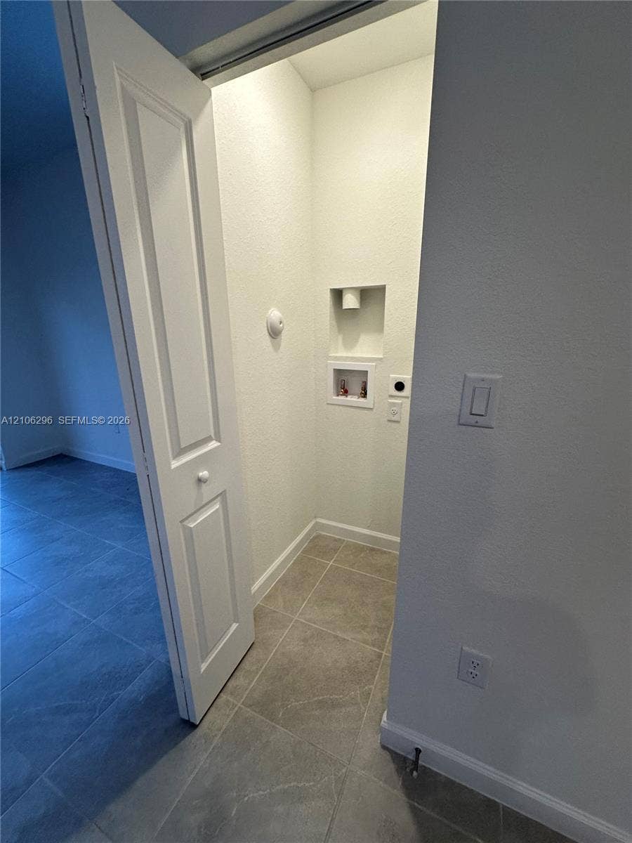 12103 NW 24th Place, #12103, Miami, Miami, FL 33167 Utility closet featuring tile flooring, a recessed plumbing connection box, and a solid-panel door