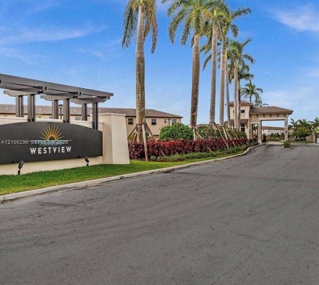 12103 NW 24th Place, #12103, Miami, Miami, FL 33167 Gated community entrance featuring a modern marquee sign, architectural pergola, stone-clad gatehouse, and rows of mature palm trees