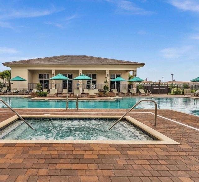 12103 NW 24th Place, #12103, Miami, Miami, FL 33167 Outdoor pool area featuring a built-in spa, paver decking, covered clubhouse structure, and stone-accented support columns