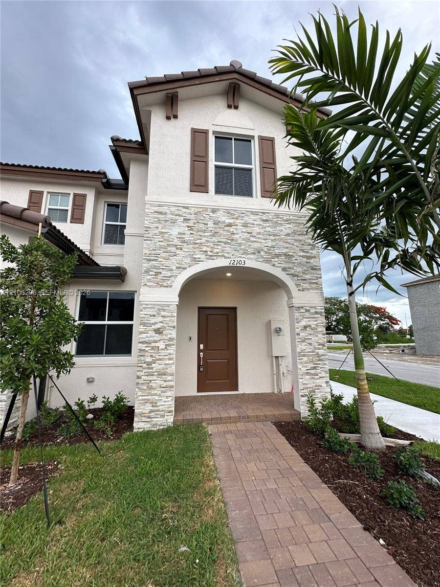 12103 NW 24th Place, #12103, Miami, Miami, FL 33167 Stucco exterior featuring stacked stone accents, decorative window shutters, an arched covered entryway, and a paved walkway