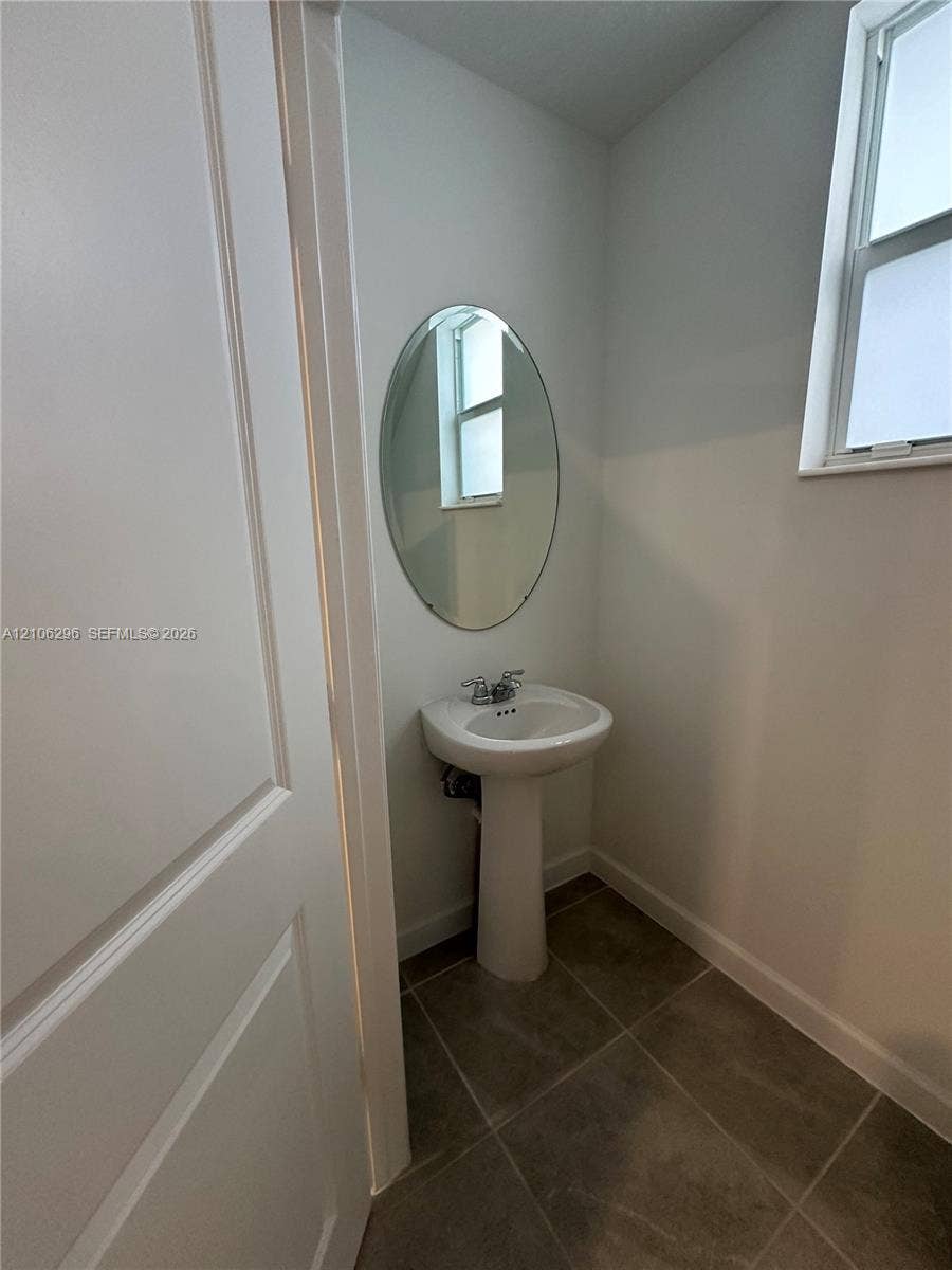 12103 NW 24th Place, #12103, Miami, Miami, FL 33167 Pedestal sink featuring a chrome faucet, oval wall-mounted mirror, and tile flooring