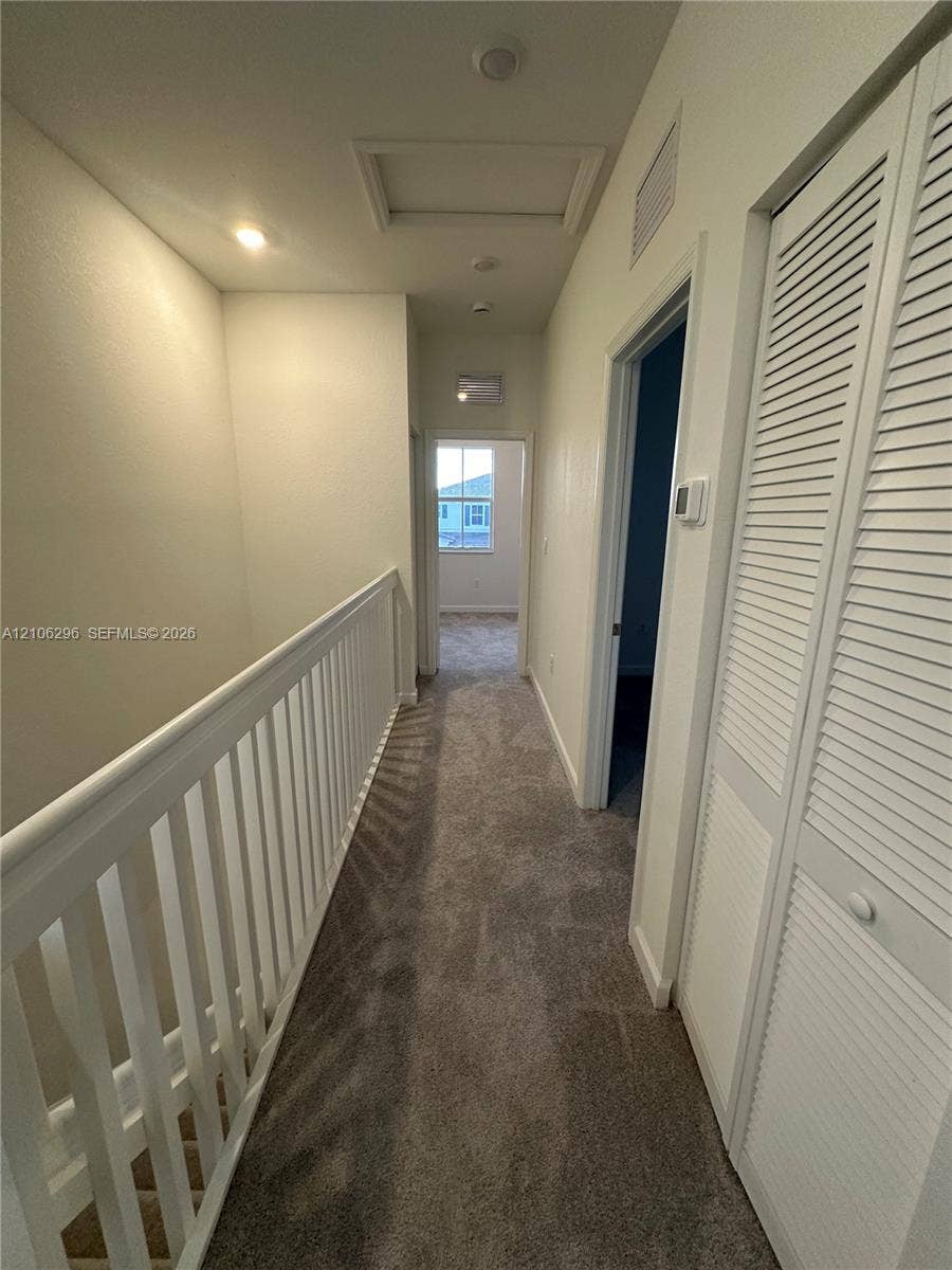 12103 NW 24th Place, #12103, Miami, Miami, FL 33167 Hallway featuring neutral wall-to-wall carpeting, white railing with vertical balusters, and louvered closet doors