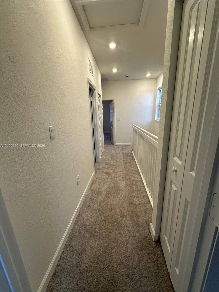12103 NW 24th Place, #12103, Miami, Miami, FL 33167 Hallway featuring neutral carpeting, recessed ceiling lighting, a white baluster railing, and louvered-panel closet doors