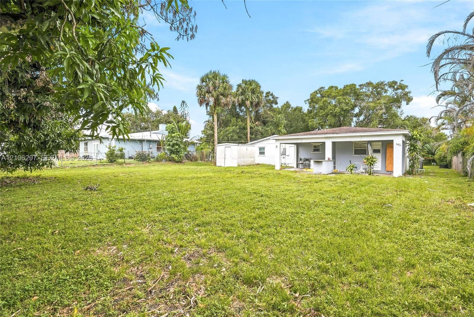4810 Lakewood Park Drive, Fort Pierce, FL 34951 Expansive backyard featuring a sprawling lawn, mature trees, a detached storage structure, and a covered patio area