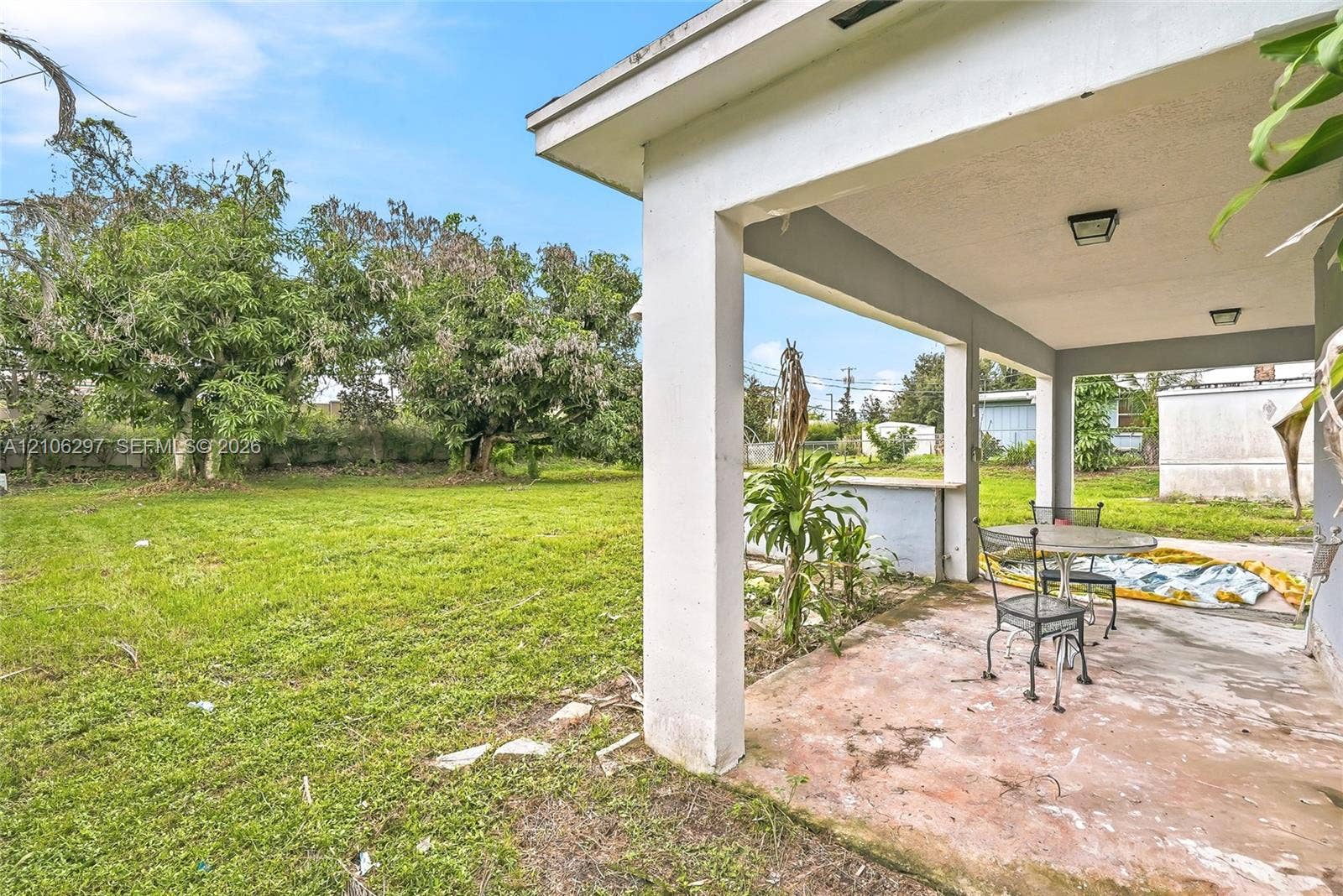 4810 Lakewood Park Drive, Fort Pierce, FL 34951 Covered concrete patio featuring structural support columns, exterior mounted lighting, and a built-in counter surface overlooking a grassy backyard with mature trees