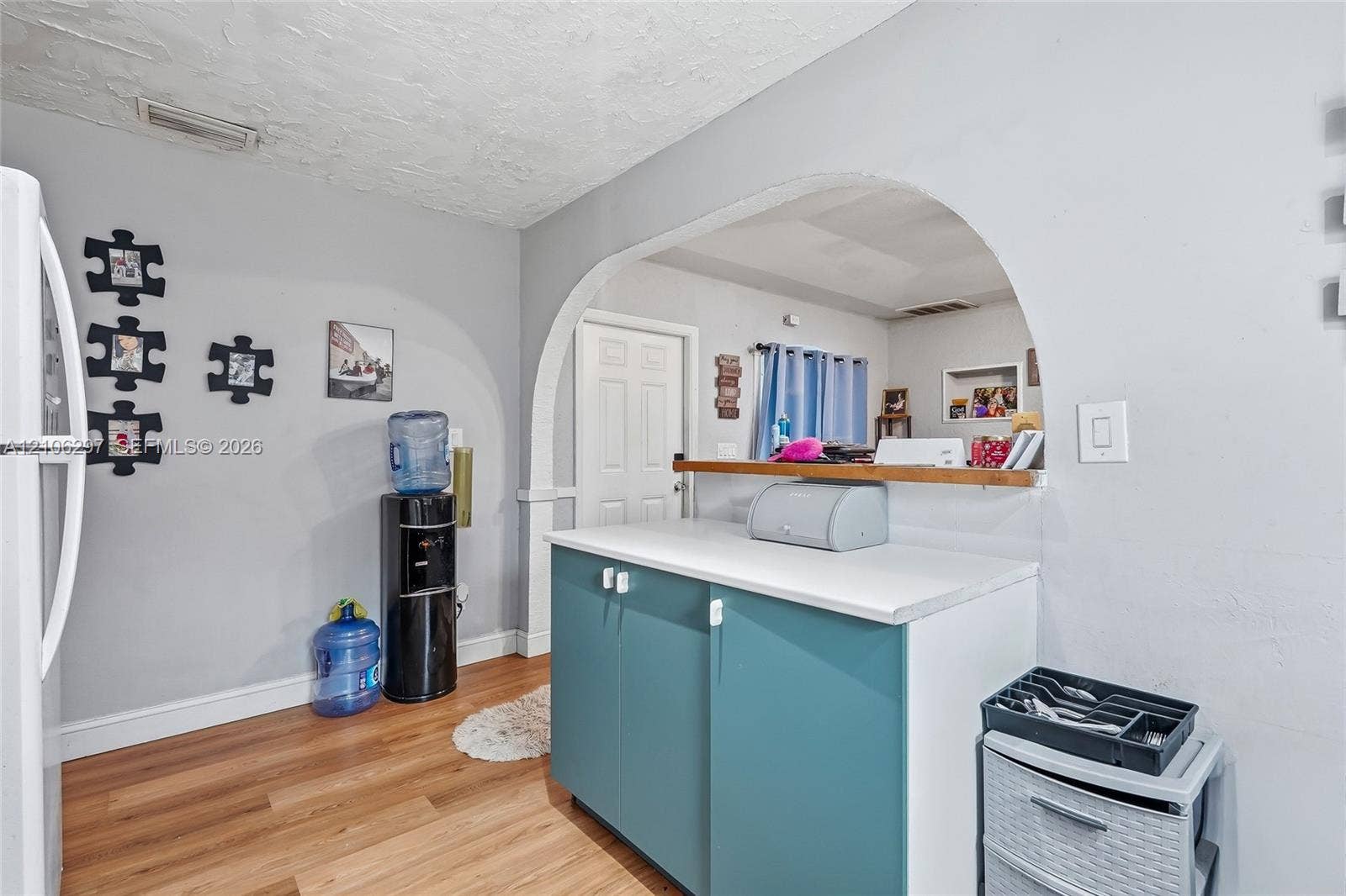 4810 Lakewood Park Drive, Fort Pierce, FL 34951 Arched wall cutout with a wooden pass-through shelf, teal-colored base cabinetry, solid surface countertop, and wood-finish flooring