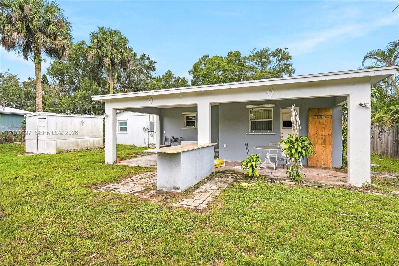 4810 Lakewood Park Drive, Fort Pierce, FL 34951 Covered concrete patio featuring an integrated masonry bar, standalone storage shed, and mature palm trees