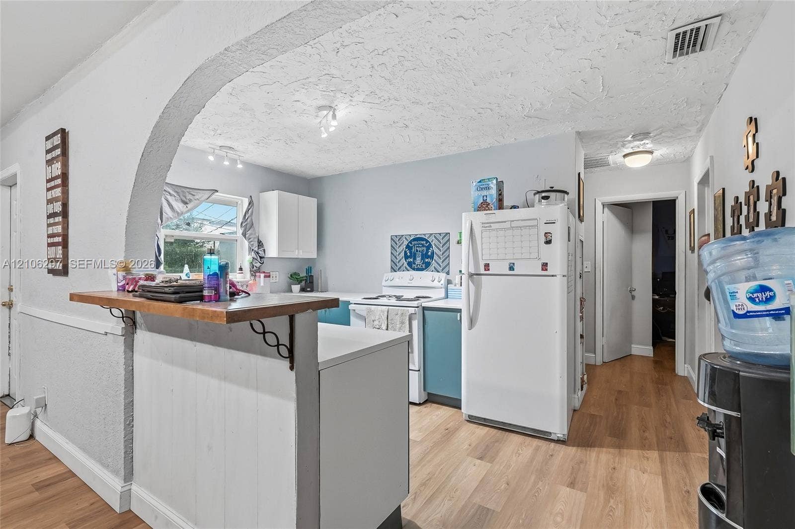 4810 Lakewood Park Drive, Fort Pierce, FL 34951 Kitchen area featuring an arched pass-through, wood-finish flooring, white upper cabinetry, and ceiling-mounted light fixtures