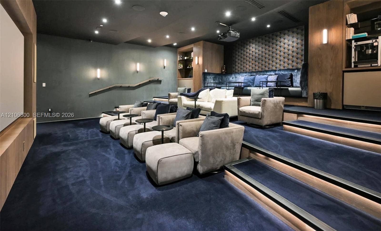 480 NE 31st Street, #1005, Miami, Miami, FL 33137 Media room featuring tiered flooring, recessed stair lighting, integrated wooden cabinetry, a projector, and wall-mounted sconce lighting