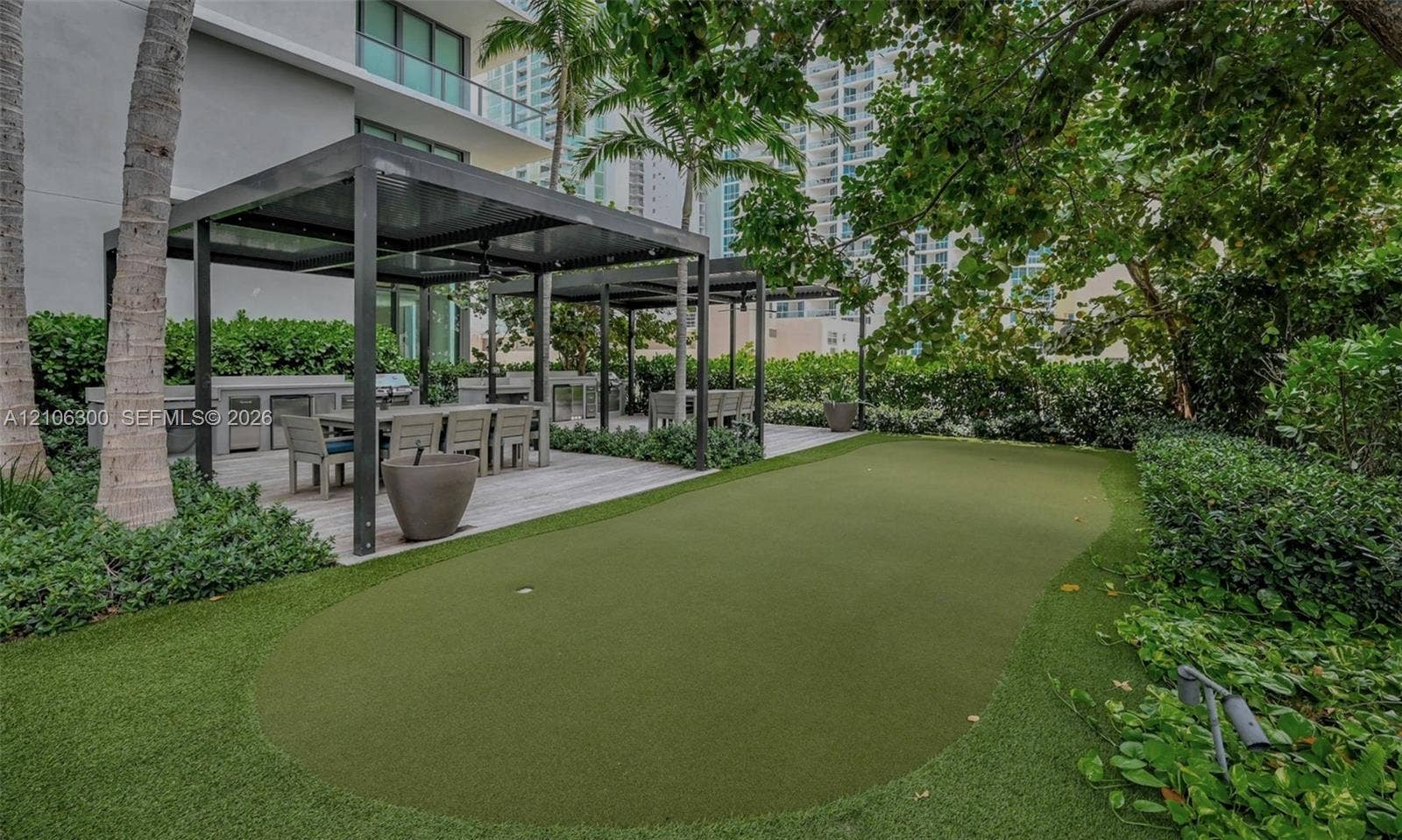 480 NE 31st Street, #1005, Miami, Miami, FL 33137 Outdoor terrace featuring a synthetic turf putting green, dual metal-framed pergolas, a built-in outdoor kitchen, and mature privacy hedges
