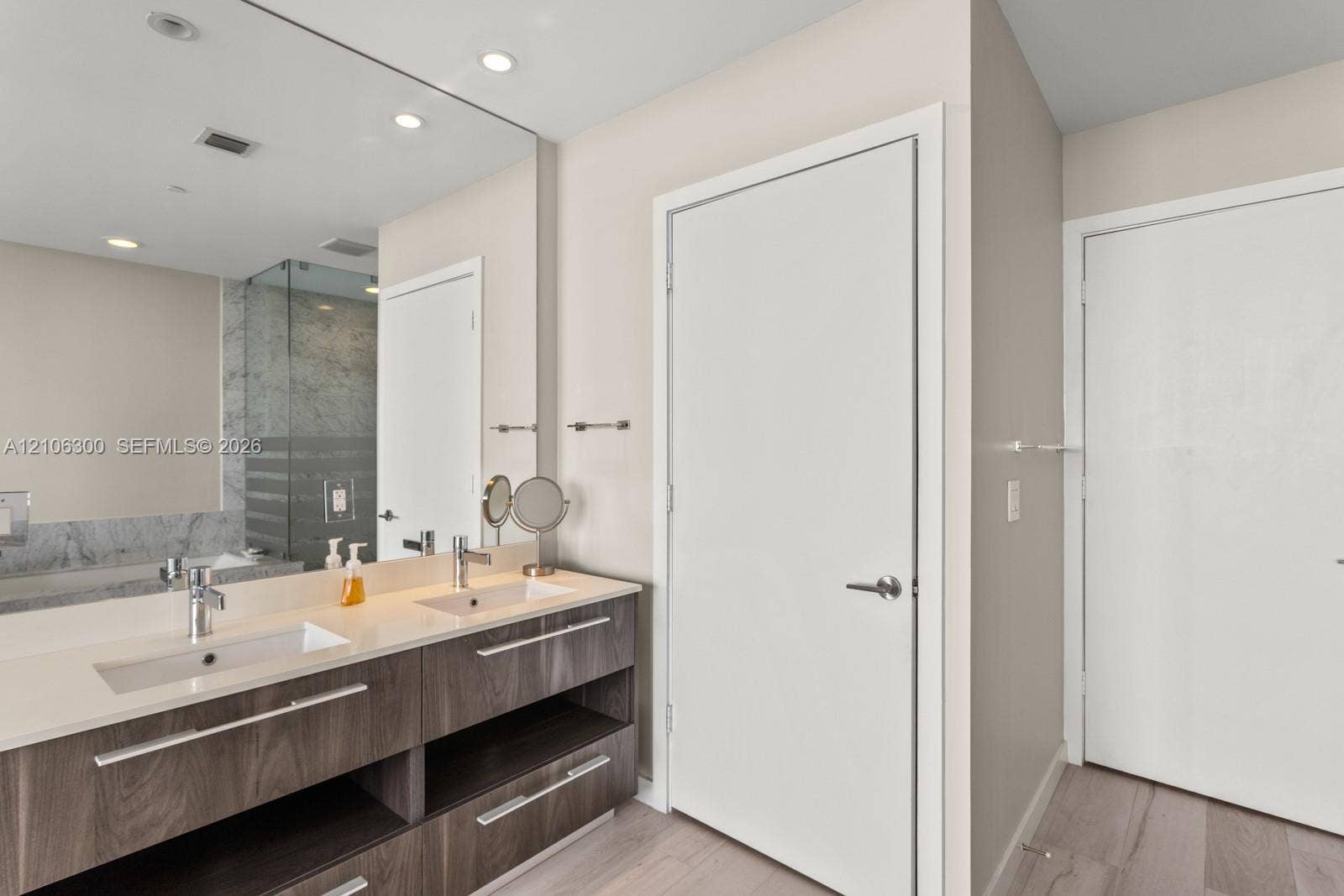 480 NE 31st Street, #1005, Miami, Miami, FL 33137 Double vanity featuring a light-toned countertop with integrated dual sinks, wood-finish cabinetry with linear hardware, full-width wall mirror, and recessed lighting
