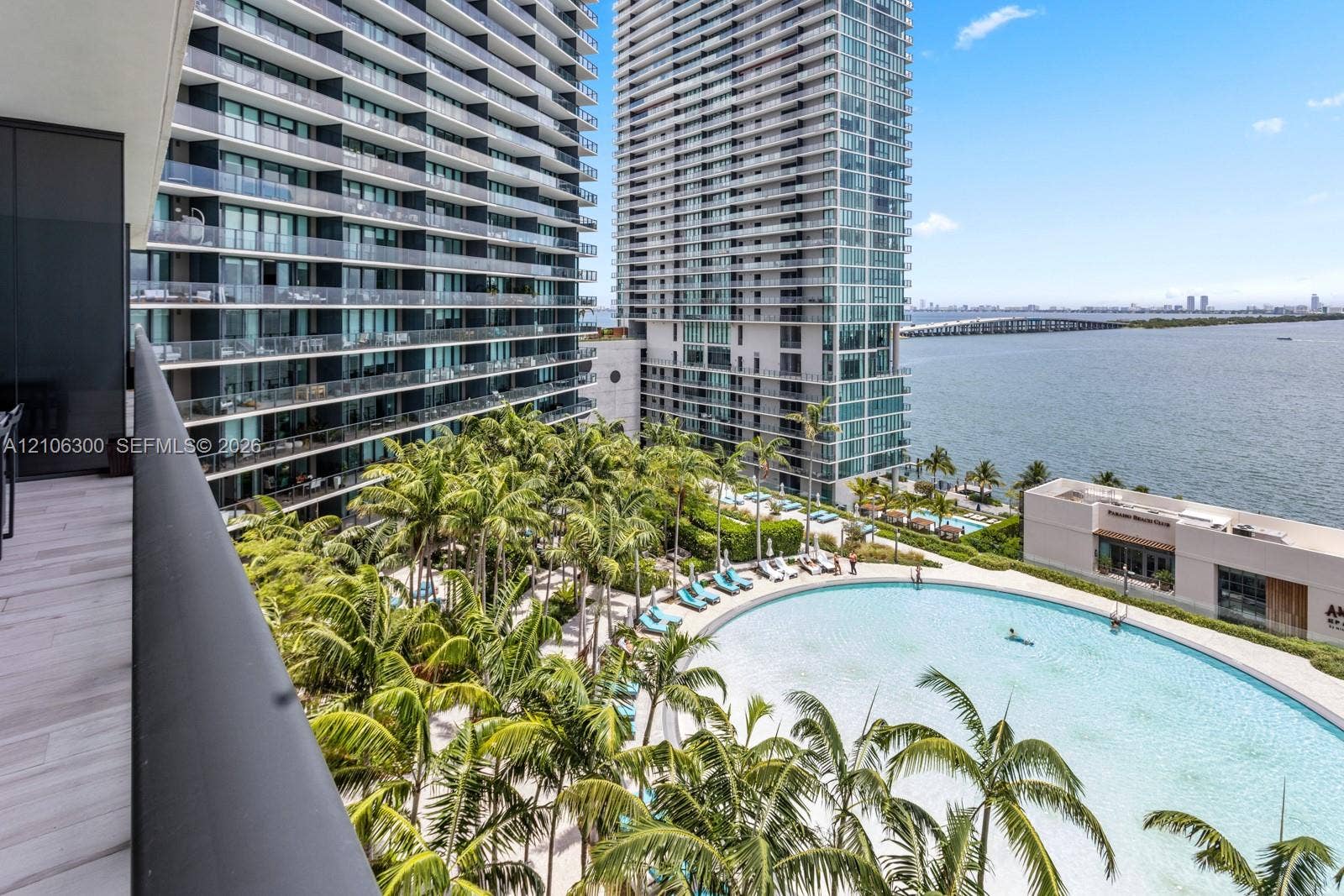 480 NE 31st Street, #1005, Miami, Miami, FL 33137 Private balcony with wood-finish flooring, overlooking a large swimming pool, landscaped palm trees, and waterfront horizon