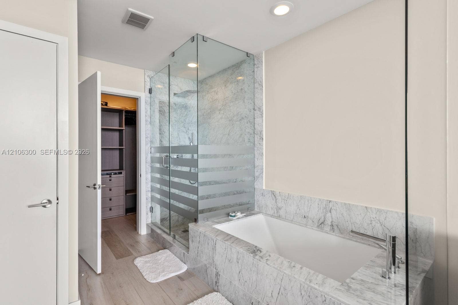 480 NE 31st Street, #1005, Miami, Miami, FL 33137 Stone-surround soaking tub with deck-mounted faucet, glass-enclosed shower, wood-finish flooring, and walk-in closet with built-in cabinetry
