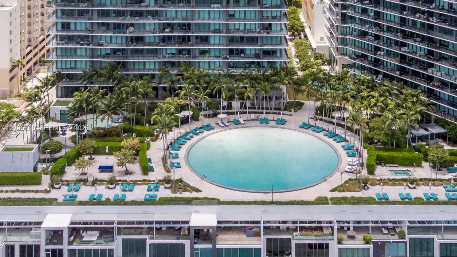 480 NE 31st Street, #1005, Miami, Miami, FL 33137 Circular swimming pool surrounded by paved decking, manicured landscaping, mature palm trees, and an integrated hot tub