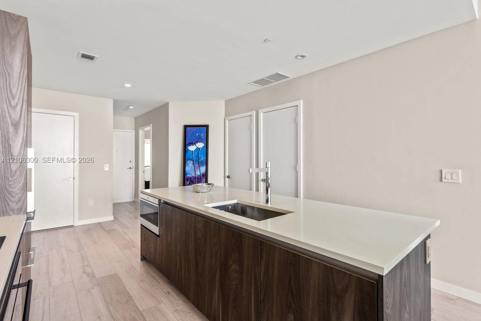 480 NE 31st Street, #1005, Miami, Miami, FL 33137 Kitchen island featuring dark wood-finish cabinetry, a white countertop, an integrated stainless steel undermount sink, and a high-arc faucet, complemented by light wood-finish flooring