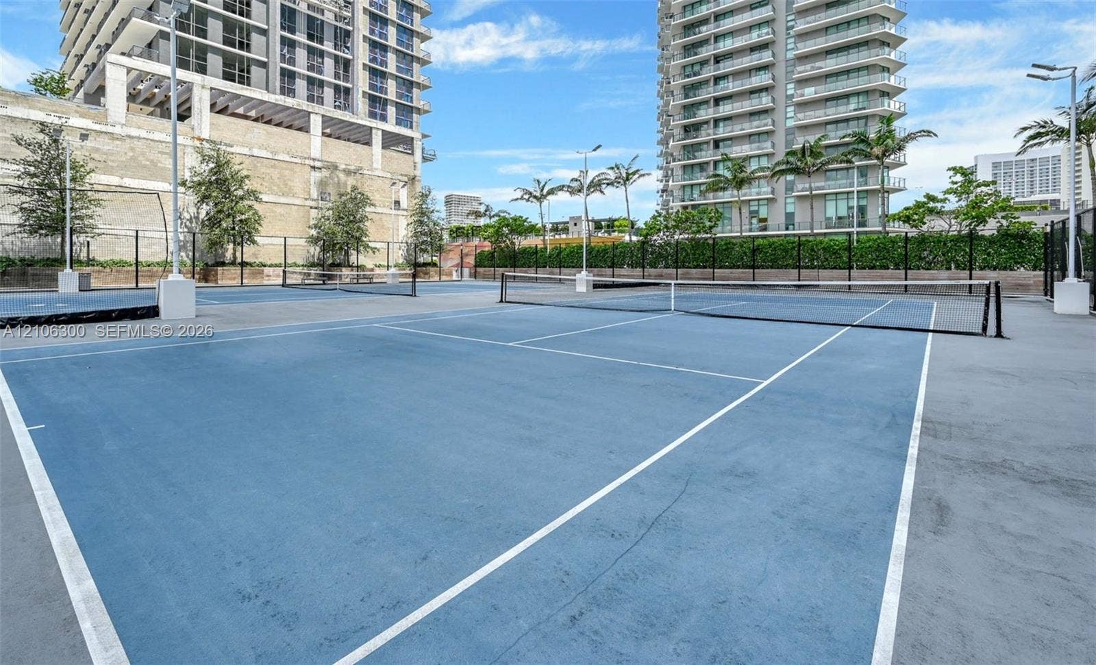 480 NE 31st Street, #1005, Miami, Miami, FL 33137 Hard-court tennis facility featuring blue acrylic surfacing, white court lines, perimeter fencing, and integrated pole-mounted lighting