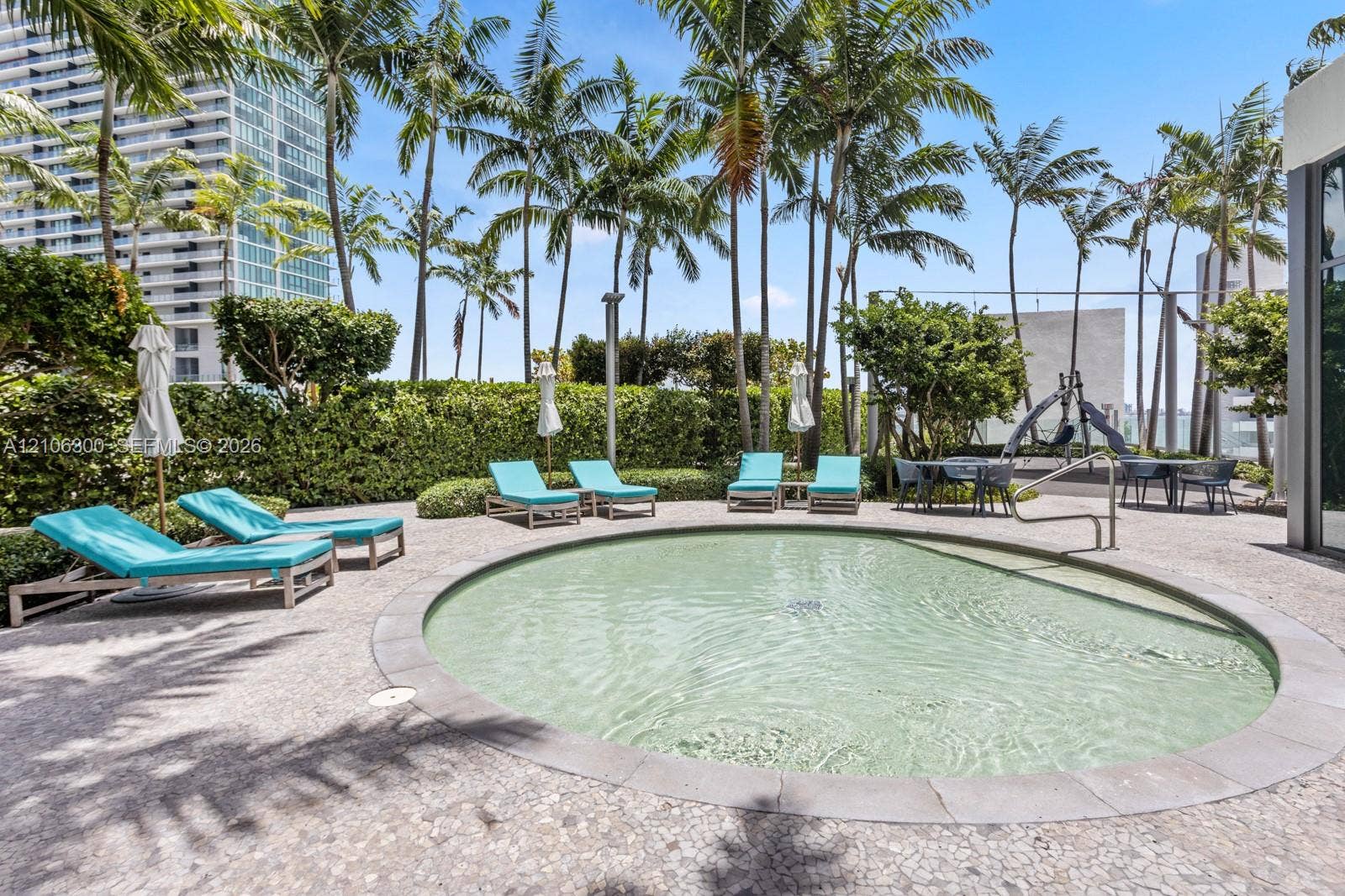 480 NE 31st Street, #1005, Miami, Miami, FL 33137 Circular swimming pool featuring a stone-tile border, set within a paved deck with mature palm trees and manicured privacy hedging