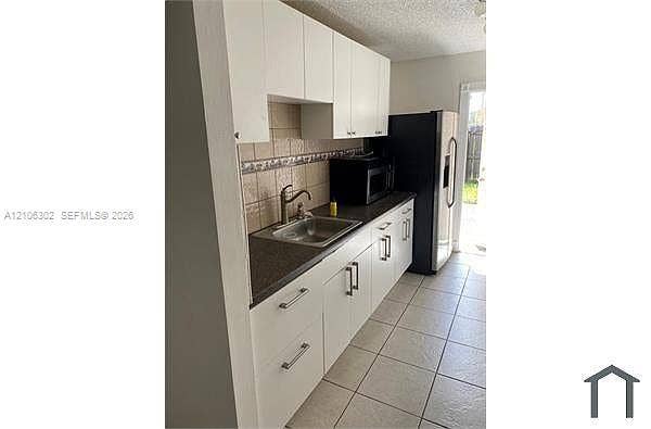 Kitchen featuring white cabinetry, dark countertops, tiled backsplash, stainless steel sink with a gooseneck faucet, and tile flooring