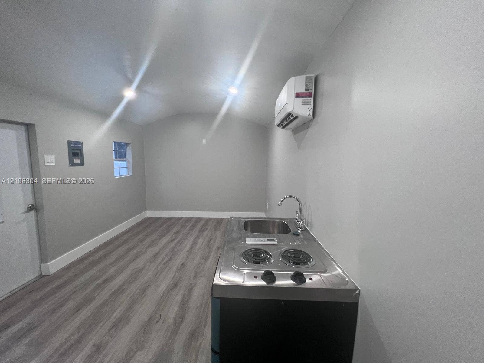 Interior space featuring wood-finish flooring, a wall-mounted ductless climate control unit, recessed ceiling lighting, and a stainless steel kitchenette unit with an integrated sink and two-burner cooktop