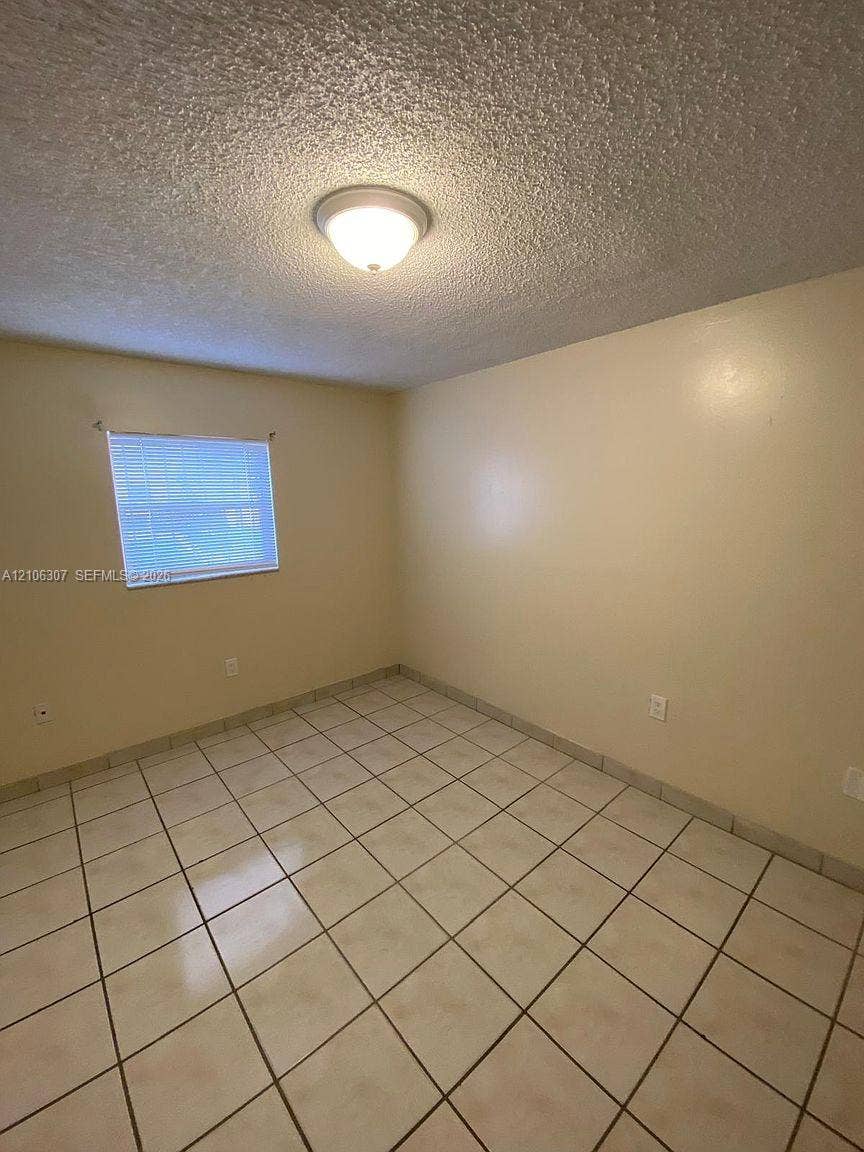 Neutral-toned room featuring ceramic tile flooring, textured ceiling finish, single-window configuration, and flush-mount lighting