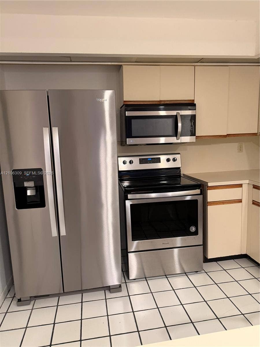 8888 SW 131st Court, #409, Miami, FL 33186 Stainless steel side-by-side refrigerator, stainless steel electric range, built-in microwave, light-toned cabinetry, and tiled flooring