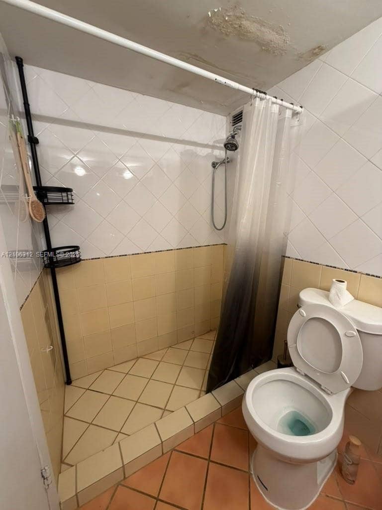 Bathroom featuring a walk-in shower with diamond-patterned tile, neutral-toned ceramic wall tile, and a standard porcelain toilet