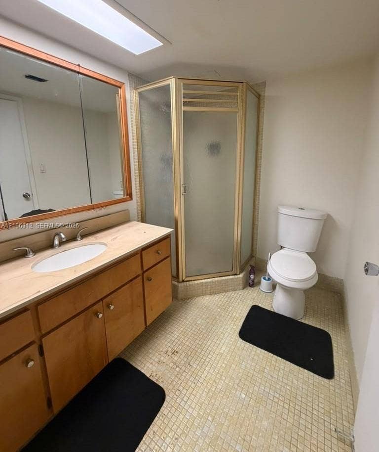 Bathroom featuring a wood-finish vanity with a stone-surfaced countertop, integrated sink, corner shower enclosure with frosted glass, and mosaic tile flooring
