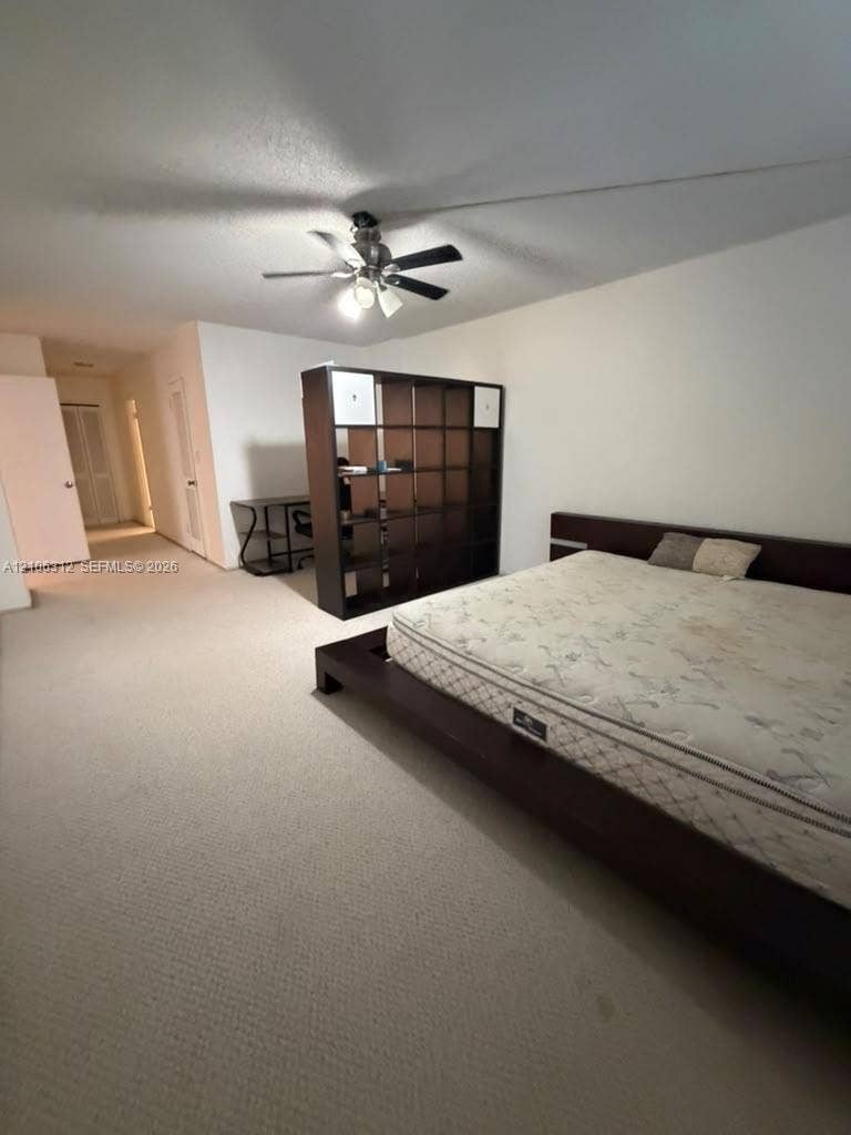 Spacious room featuring neutral carpeting and a ceiling-mounted light fixture with a multi-blade fan