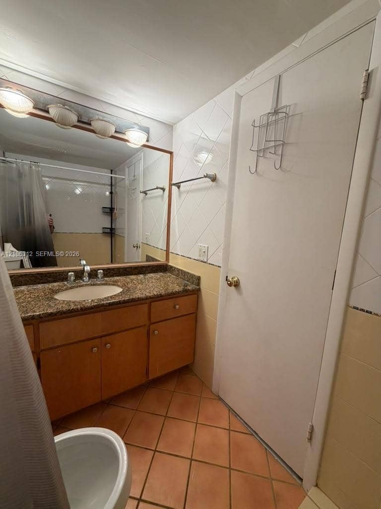 800 NE 195th Street, #311, Miami, Miami, FL 33179 Bathroom featuring a wood vanity with a stone countertop, oval undermount sink, multi-bulb wall lighting, and tile flooring