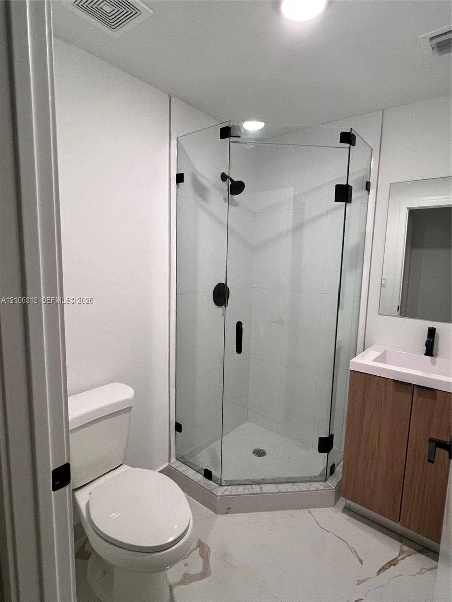 14508 SW 260th Street, #14508, Homestead, Homestead, FL 33032 Corner shower stall with a frameless glass enclosure and matte black hardware, vanity with wood-finish cabinetry and rectangular sink, and stone-finish tile flooring