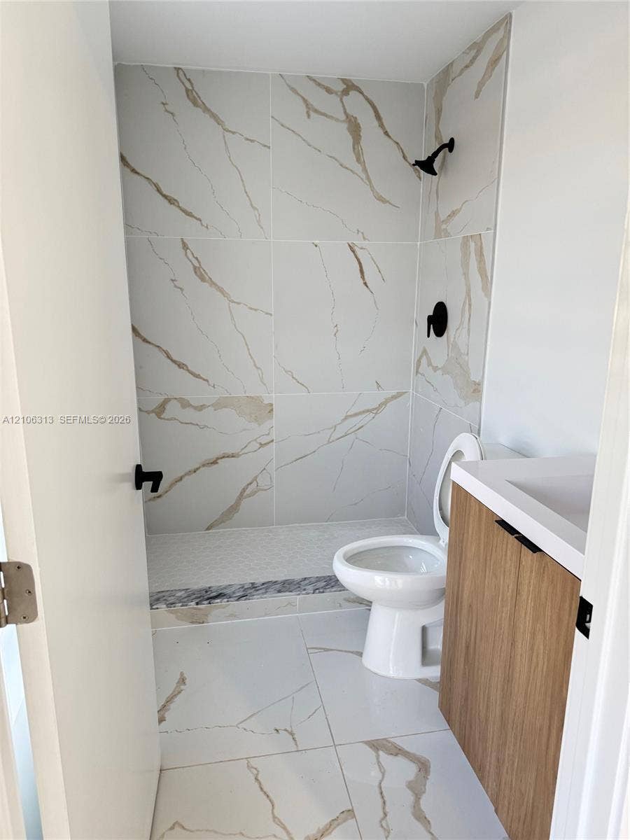 14508 SW 260th Street, #14508, Homestead, Homestead, FL 33032 Large-format stone-patterned floor and wall tile, wood-finish vanity with a built-in sink, walk-in shower with mosaic tile flooring, and matte black plumbing fixtures