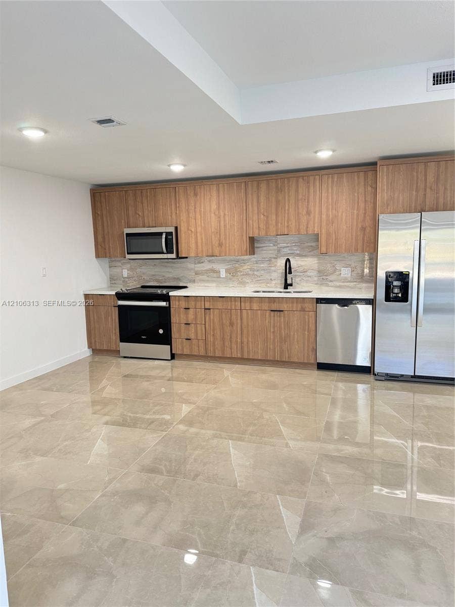 14508 SW 260th Street, #14508, Homestead, Homestead, FL 33032 Kitchen featuring flat-panel wood cabinetry, light stone-finish countertops, stainless steel appliances, a matte black faucet, and large-format tile flooring