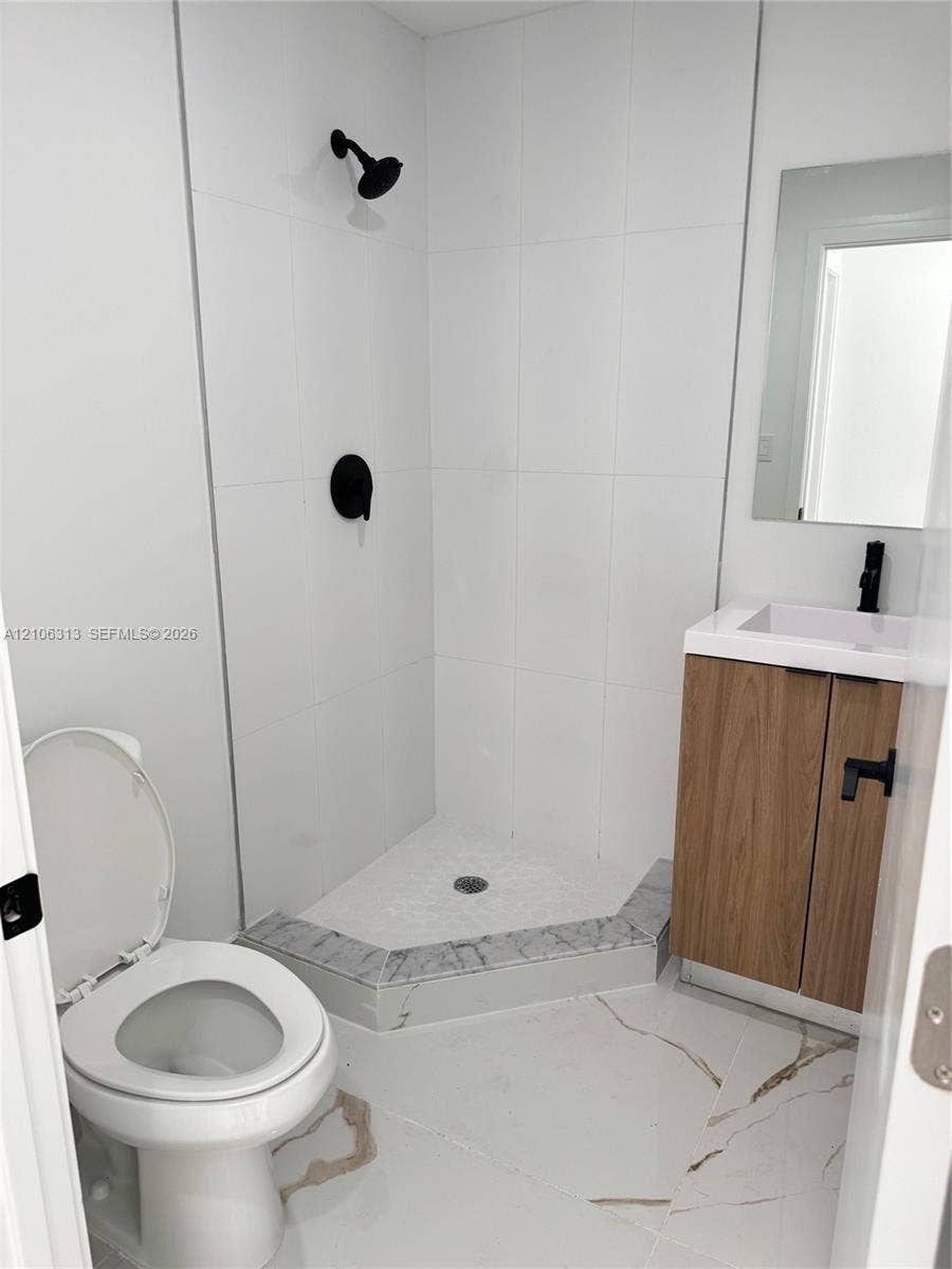 14508 SW 260th Street, #14508, Homestead, Homestead, FL 33032 Corner shower with floor-to-ceiling white tile, wood-finish vanity, stone-patterned floor tile, matte black fixtures, and a frameless mirror
