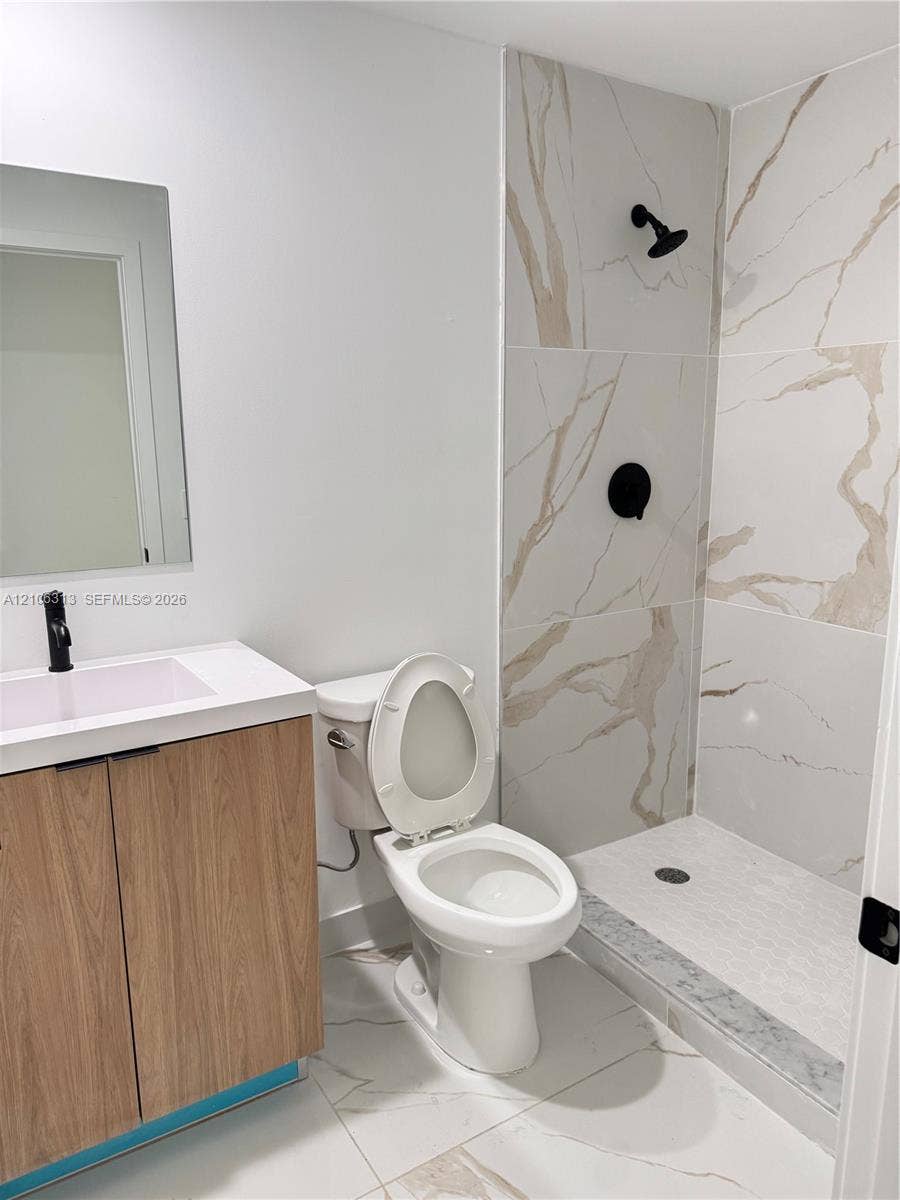 14508 SW 260th Street, #14508, Homestead, Homestead, FL 33032 Bathroom featuring a vanity with a light wood-finish cabinet and solid-surface countertop, a frameless mirror, large-format tile flooring, and a walk-in shower with veined wall tile and matte black fixtures