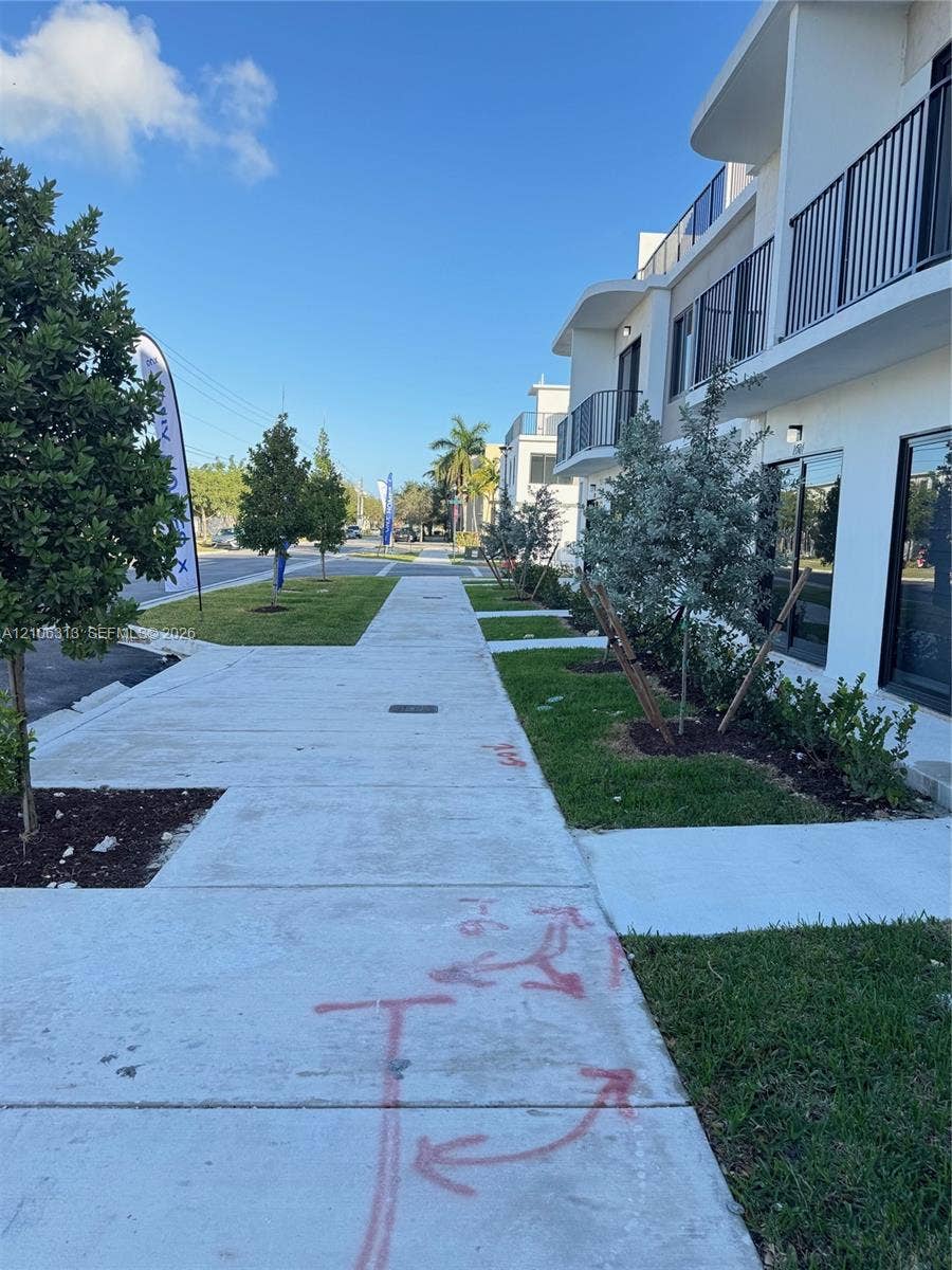 14508 SW 260th Street, #14508, Homestead, Homestead, FL 33032 Multi-story building exterior featuring white stucco facade, metal balcony railings, expansive glass windows, concrete sidewalk, and manicured landscaping