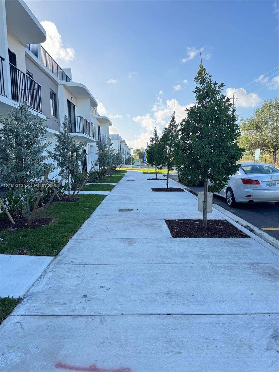 14508 SW 260th Street, #14508, Homestead, Homestead, FL 33032 Multi-story exterior featuring a modern facade with rounded architectural accents, integrated metal balcony railings, concrete sidewalk, and landscaped tree-lined beds