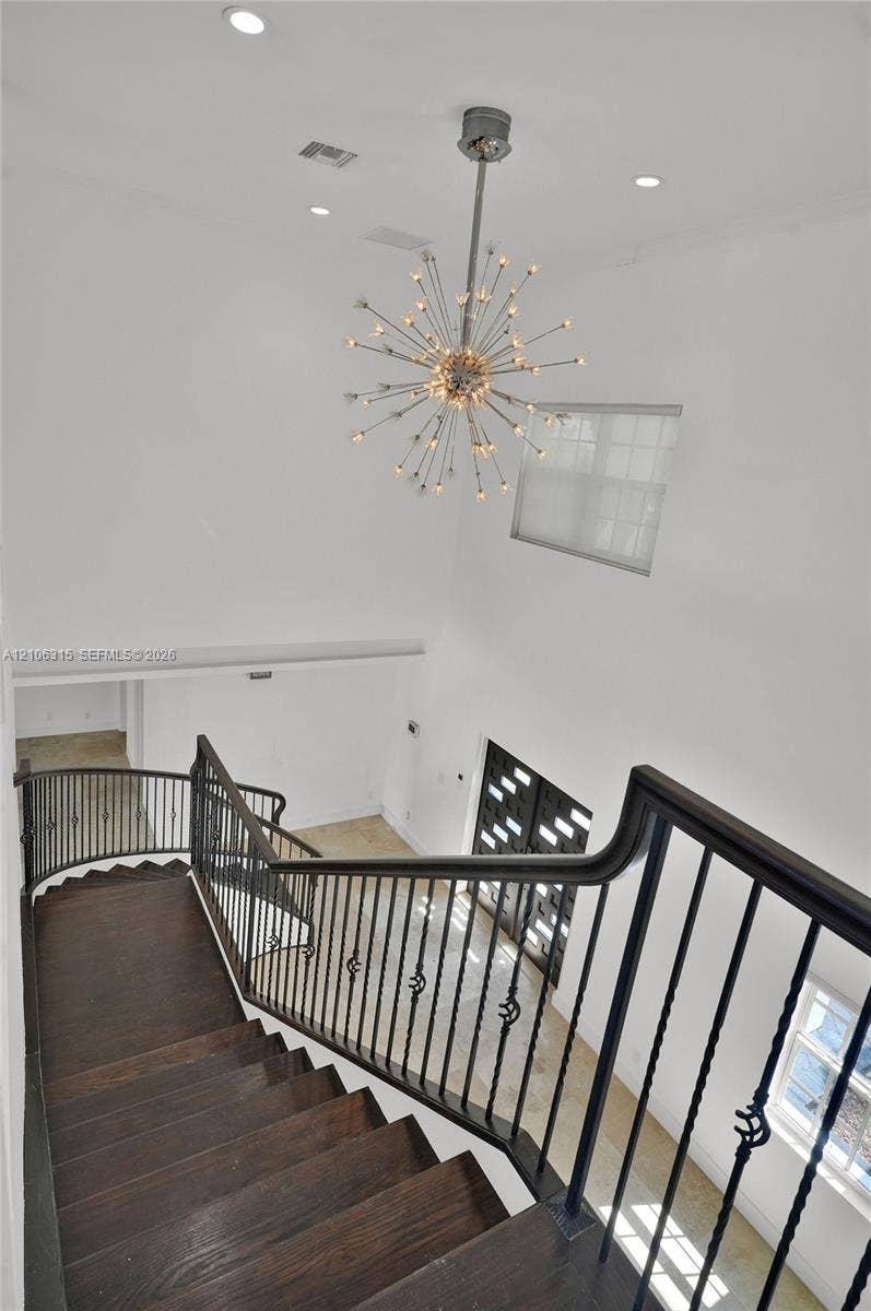 2319 NE 35th Drive, Fort Lauderdale, FL 33308 Staircase featuring dark wood-finish treads and a decorative metal railing, highlighted by a multi-point sputnik-style chandelier, recessed lighting, and high-ceiling architecture