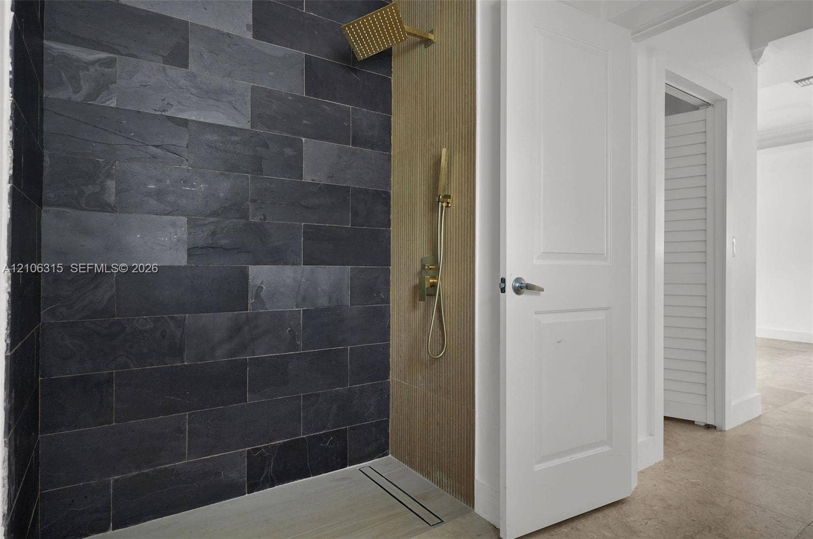 2319 NE 35th Drive, Fort Lauderdale, FL 33308 Walk-in shower featuring charcoal-toned stone tile, vertical wood-finish paneling, brushed metallic rainfall shower head with handheld sprayer, and a linear floor drain