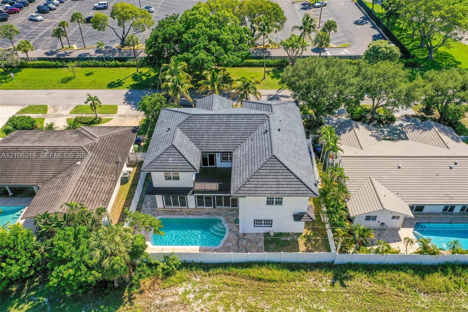 2319 NE 35th Drive, Fort Lauderdale, FL 33308 Two-story residence featuring a dark-toned tile roof, exterior stucco finish, private swimming pool, and stone-paver pool deck enclosed by white perimeter fencing