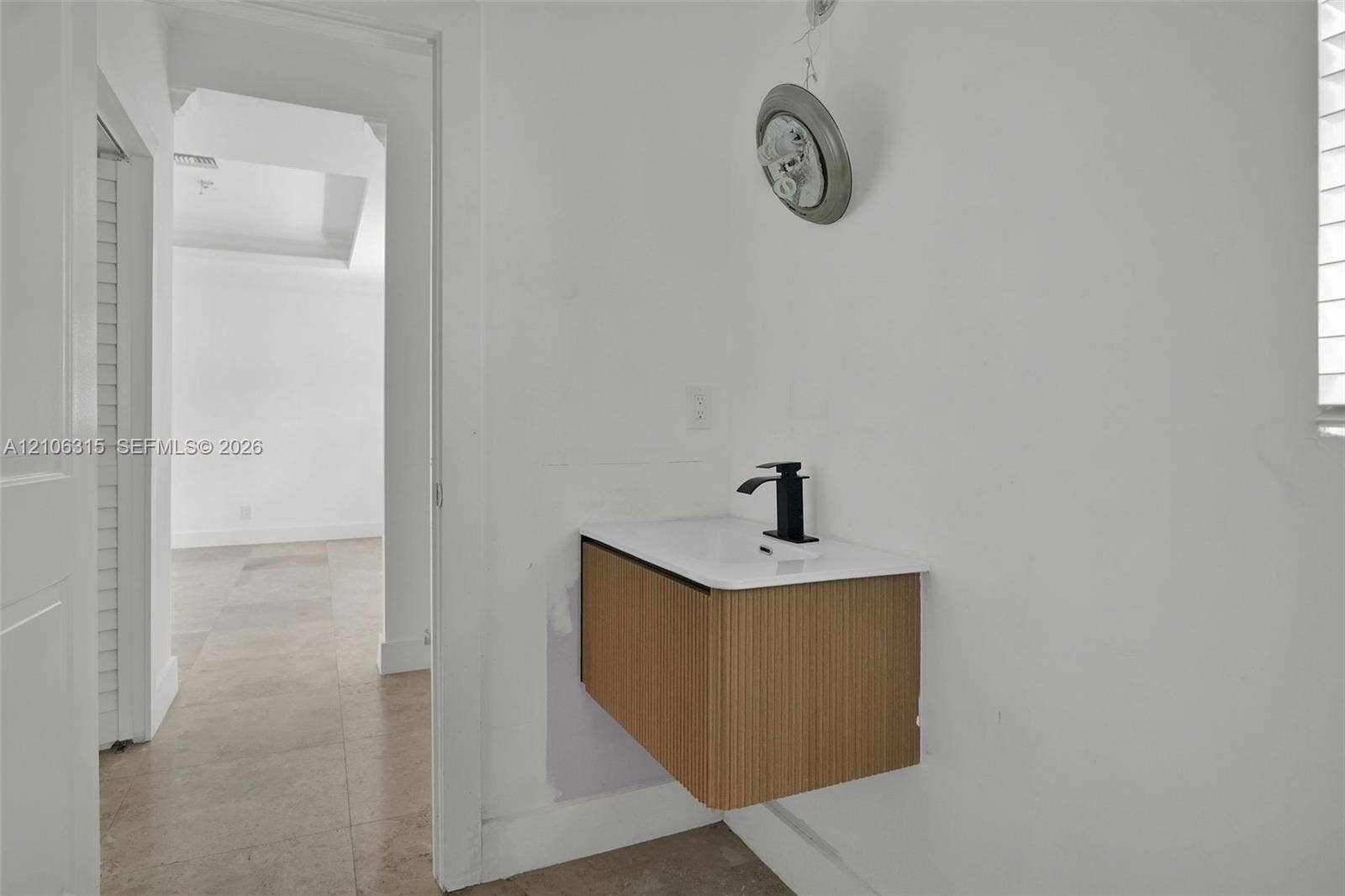 2319 NE 35th Drive, Fort Lauderdale, FL 33308 Wall-mounted floating vanity with reeded wood-finish cabinetry, white countertop, and matte black single-handle faucet