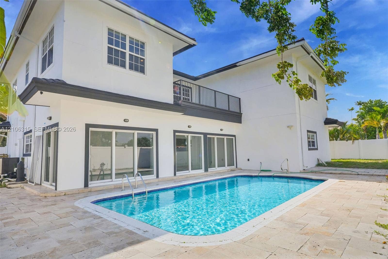 2319 NE 35th Drive, Fort Lauderdale, FL 33308 Two-story exterior featuring white stucco finish, second-level balcony with metal railing, multiple sliding glass doors, and a rectangular swimming pool surrounded by stone-tile patio