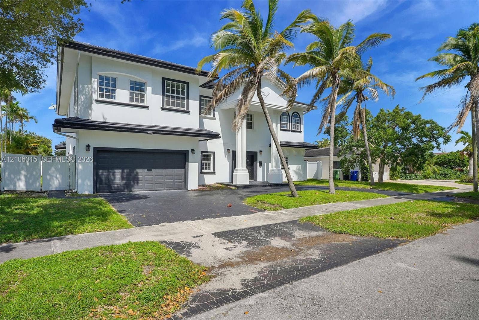 2319 NE 35th Drive, Fort Lauderdale, FL 33308 Two-story residence featuring a white exterior, multi-pane windows, a covered entryway with structural columns, an attached two-car garage, and mature palm trees