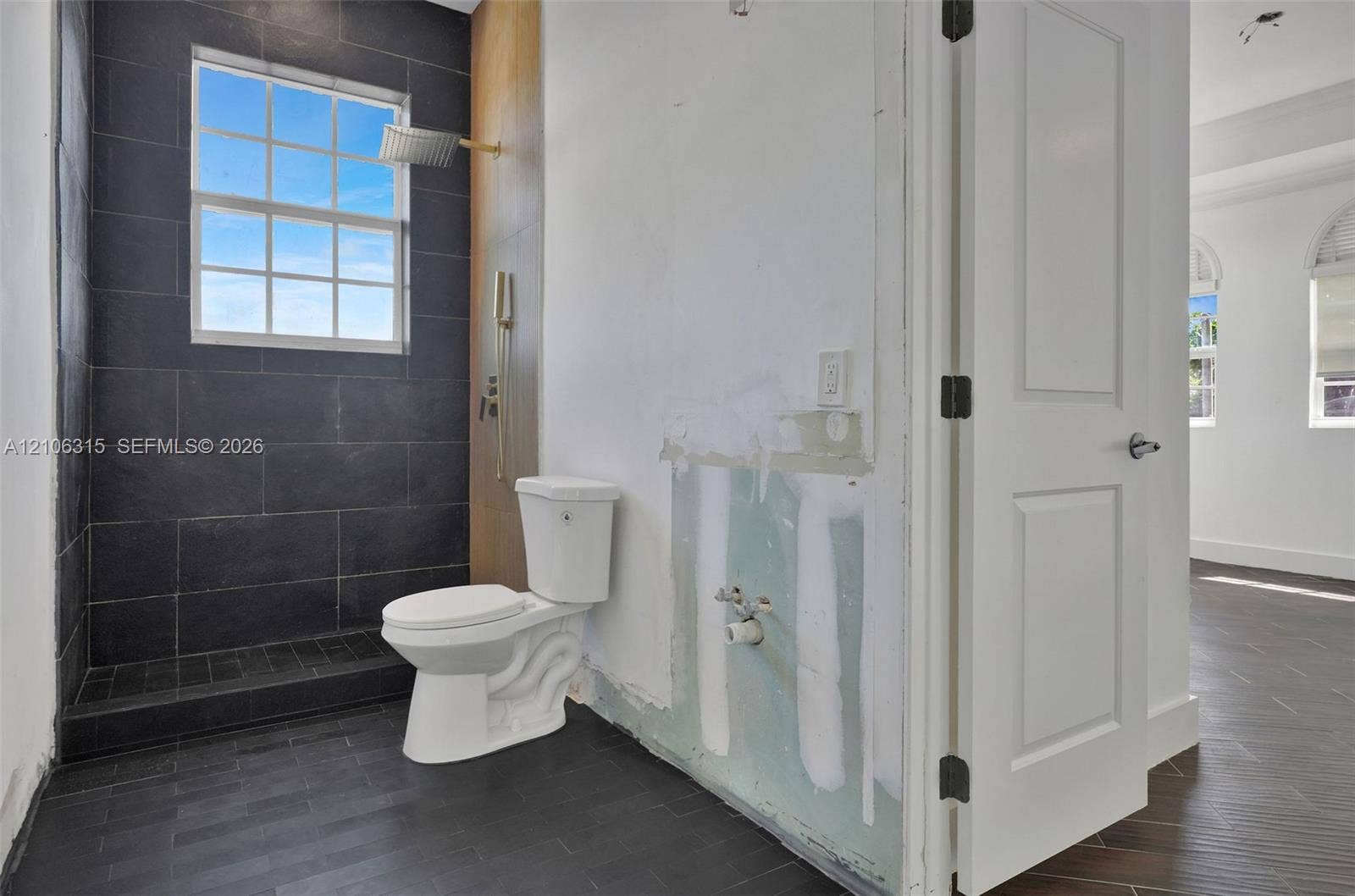2319 NE 35th Drive, Fort Lauderdale, FL 33308 Walk-in shower enclosure with large-format dark tile, wall-mounted rain shower head, dual-pane grid window, and wood-finish flooring