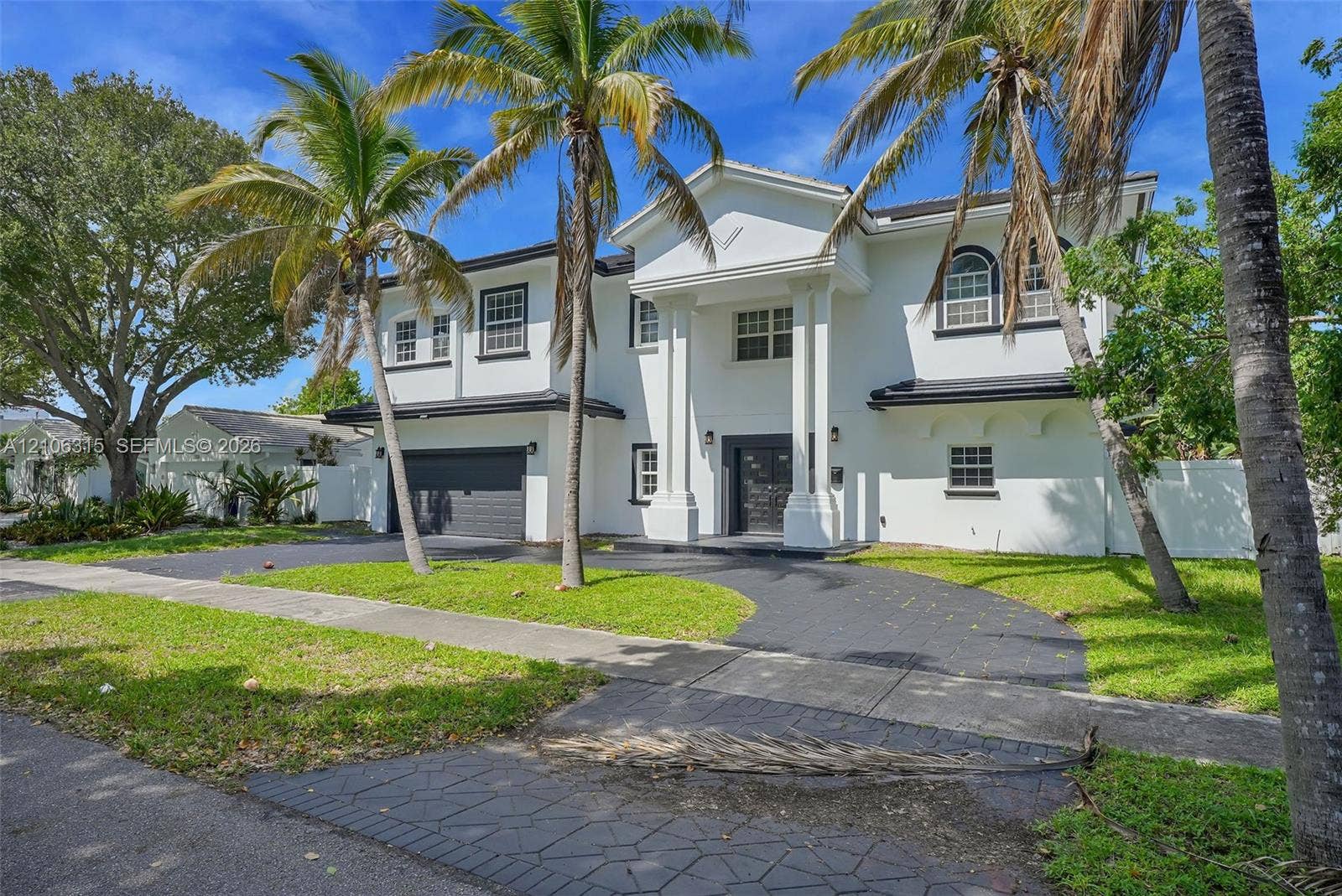2319 NE 35th Drive, Fort Lauderdale, FL 33308 Two-story exterior featuring a white stucco facade, arched windows, covered entryway with classical columns, and a stamped concrete driveway