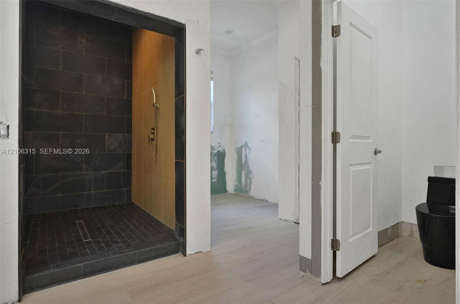 2319 NE 35th Drive, Fort Lauderdale, FL 33308 Walk-in shower with dark large-format tile surround, integrated linear drain, wall-mounted handheld shower fixture, light wood-finish flooring, and black toilet