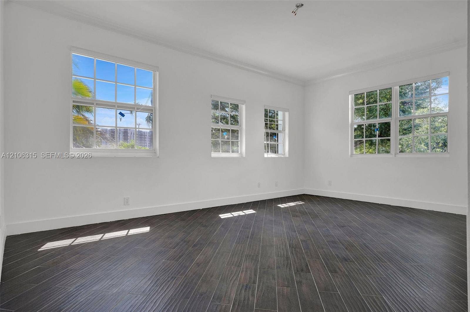 2319 NE 35th Drive, Fort Lauderdale, FL 33308 Interior space featuring dark wood-finish flooring, white walls, and multiple multi-pane windows with grid detailing