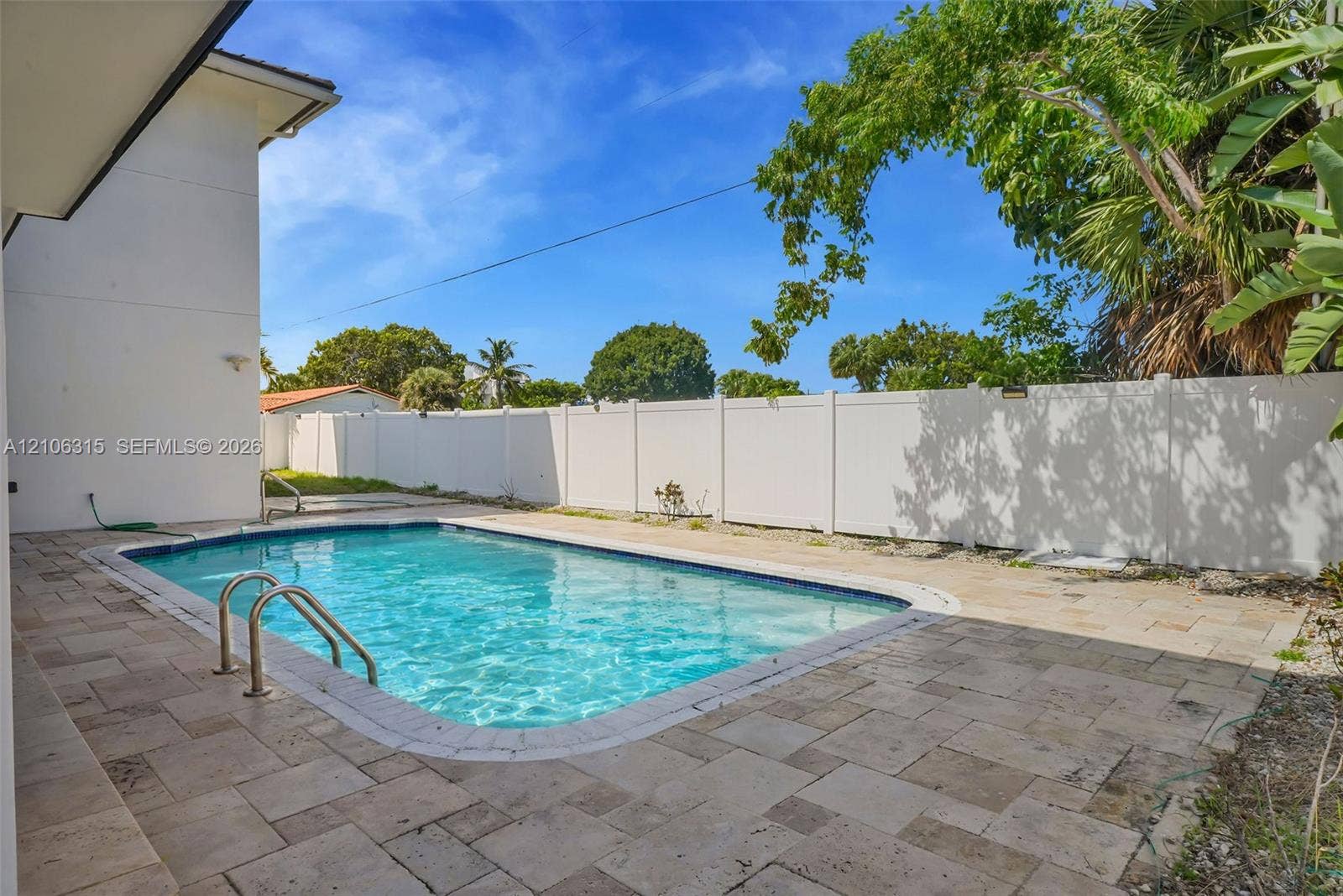 2319 NE 35th Drive, Fort Lauderdale, FL 33308 In-ground swimming pool with metal ladder, surrounded by stone paver patio and enclosed by a solid vinyl privacy fence